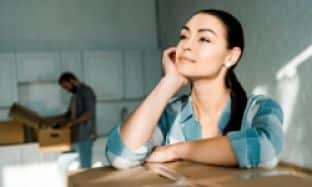 Woman Enjoying Her Moving Day While Her Husband Unpacks In The Background - Stress Free Moving