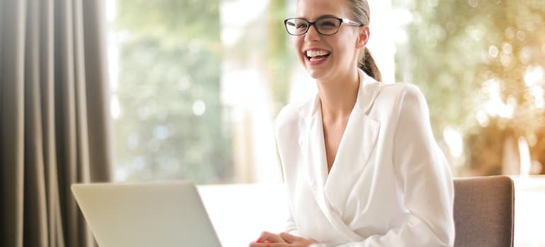 A woman smiling while using her laptop to research moving from Connecticut to Maryland