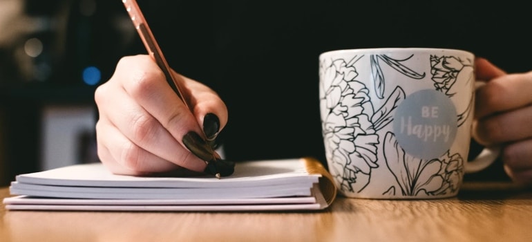 Person writing and drinking a hot drink 