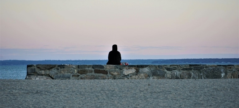 Person sitting at a beach trying to adjust to life in Stamford after moving from a big city