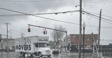 A Collegian Movers truck driving on wet streets in New Haven, CT, illustrating rainy weather conditions and seasonal challenges for relocation.