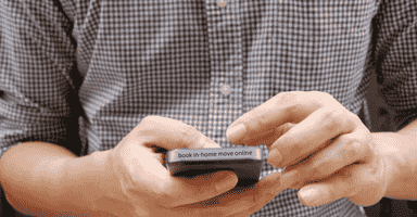 Man in plaid shirt booking an in home move on his cellphone.