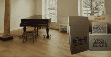 Baby grand piano on piano dolly in empty room with Collegian Movers boxes.